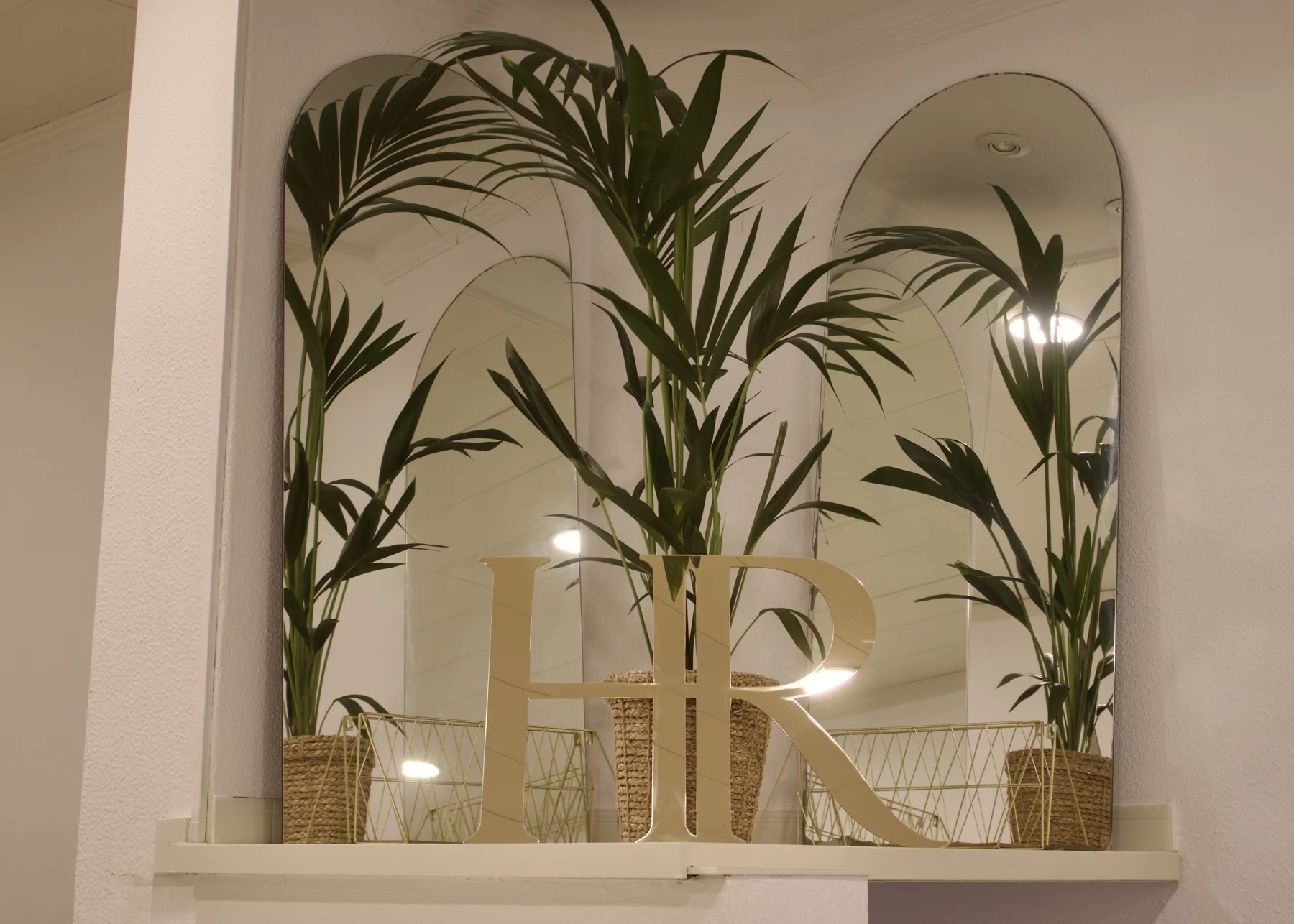 Pormenor do espaço HR com espelhos, plantas e monograma dourado